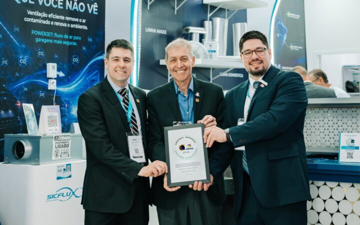 Paulo Macedo, presidente executivo da ABRAVA (ao centro), entrega o selo aos diretores Marcelo Munhoz (à esq.) e Rafael Munhoz (à dir.) da Sicflux, no estande da empresa na Febrava Rio 2026.