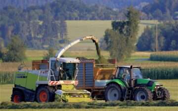 Colhedora de forragem descarrega silagem em carreta puxada por trator durante a colheita no campo.